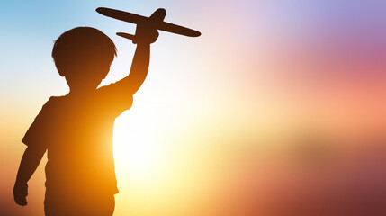 Silhouette of a boy playing with toy airplane on sunset background