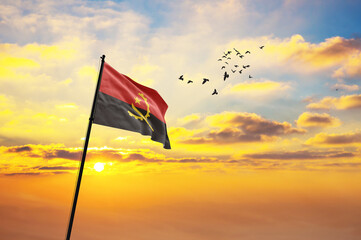 Waving flag of Angola against the background of a sunset or sunrise. Angola flag for Independence...