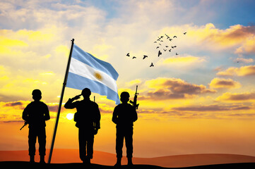 Silhouettes of soldiers with the Argentina flag stand against the background of a sunset or...