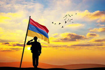 Silhouette of a soldier with the Armenia flag stands against the background of a sunset or sunrise....