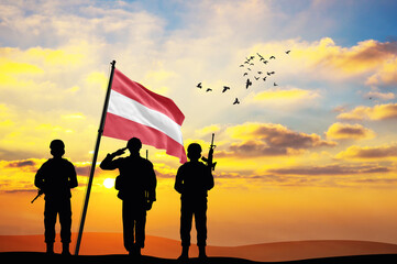Silhouettes of soldiers with the Austria flag stand against the background of a sunset or sunrise....