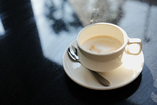 Close-up A cup of coffee on black  table with morning sunshing to the cou ,coffee with cappuccino milk steam in white cup.