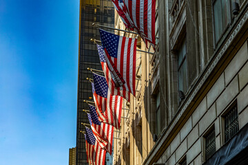 The American flags waving on the skyscrapers of Fifth Avenue, in the heart of Manhattan and the heart of the Big Apple in New York, USA, under a splendid sunny day and blue sky.