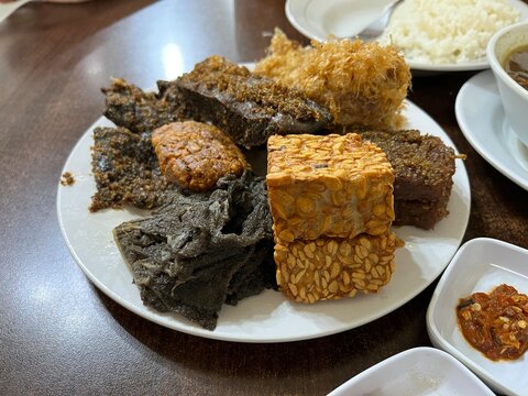 A plate of side dish consists of fried tempeh, cow beef, Potato Perkedel, and Empal in a restaurant