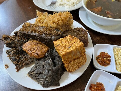 A plate of side dish consists of fried tempeh, cow beef, Potato Perkedel, and Empal in a restaurant