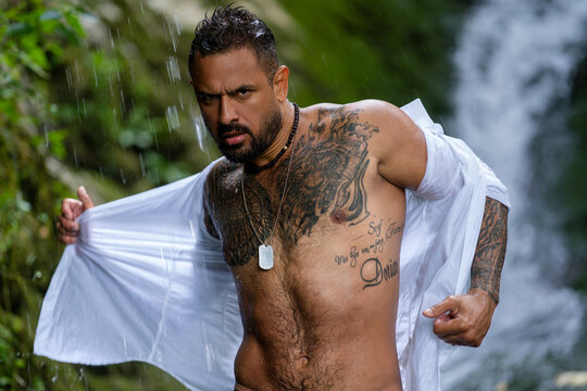 Sexy naked muscular Hispanic man sexy posing outdoor. Sexy man in Alps waterfall. Man freedom lifestyle in nature. Sexy Hispanic guy summer on nature. Man undress shirt under mountain river waterfall. - Powered by Adobe