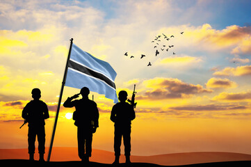 Silhouettes of soldiers with the Botswana flag stand against the background of a sunset or sunrise....