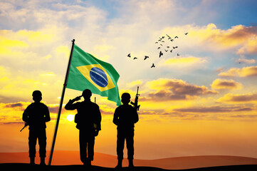 Silhouettes of soldiers with the Brazil flag stand against the background of a sunset or sunrise....