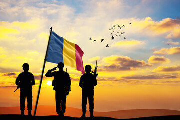 Silhouettes of soldiers with the Chad flag stand against the background of a sunset or sunrise....