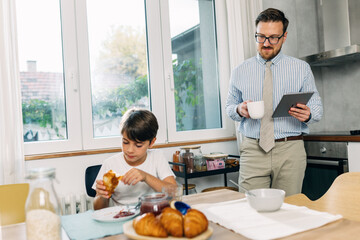 Businessman is watching his son having breakfast.