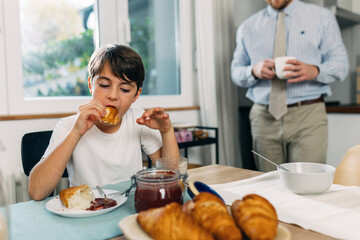 Obraz na płótnie Canvas Cute young Caucasian boy eating a croissant with jam for breakfast.