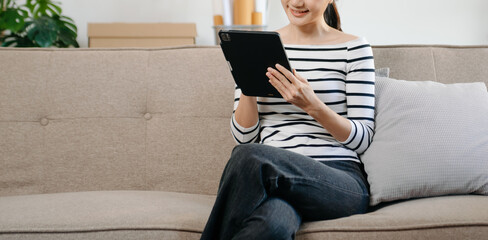 Young asian woman using smartphone and tablet while seated on couch at home.