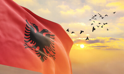 Waving flag of Albania against the background of a sunset or sunrise. Albania flag for Independence Day. The symbol of the state on wavy fabric. - obrazy, fototapety, plakaty