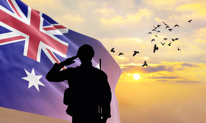 Silhouette of a soldier with the Australia flag stands against the background of a sunset or sunrise. Concept of national holidays. Commemoration Day. - obrazy, fototapety, plakaty