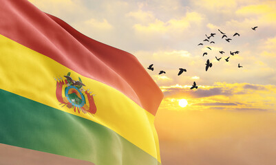 Waving flag of Bolivia against the background of a sunset or sunrise. Bolivia flag for Independence Day. The symbol of the state on wavy fabric. - obrazy, fototapety, plakaty
