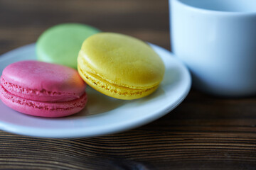 Multicolored macaroons on a white plate on a wooden table. The concept is a coffee break. Selective focus, shallow depth of field.