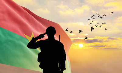 Silhouette of a soldier with the Burkina Faso flag stands against the background of a sunset or...