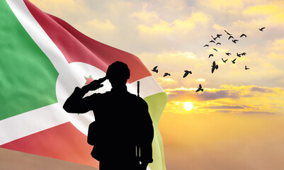 Silhouette of a soldier with the Burundi flag stands against the background of a sunset or sunrise....