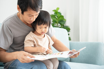 Happy Asian father relax and read book with baby time together at home. parent sit on sofa with daughter and reading a story. learn development, childcare, laughing, education, storytelling, practice.