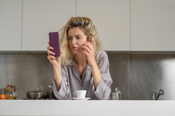 Tired unhappy woman chatting on mobile phone on kitchen at home. Housewife mood in the morning.