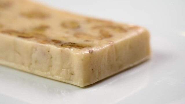 Traditional Spanish Christmas Turron with almond and nougat on a white ceramic dish close up. Rotation