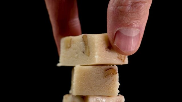 Spanish Christmas Turron with almond and nougat on a black background. Hand taking single sweet slice close up
