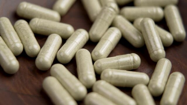 Herbal supplement vitamin capsules falling into a wooden bowl. Prescription natural pills. Herb medicine tablets