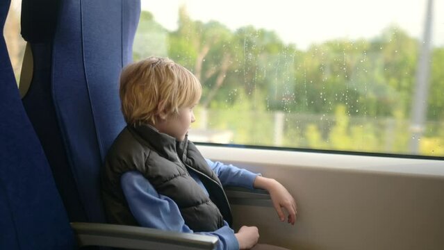 Cute preteen boy is traveling in a local train carriage or by railroad while it rain outside. Portrait of child passenger.