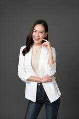Asian female executive with long hair Pose for photos like a professional model. In a studio with a gray background, wearing a white suit, long jeans, smiling cutely, wearing a gold necklace.