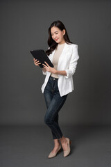 Full body photo of long-haired Asian female executive, company owner. Smiling and using a tablet to...