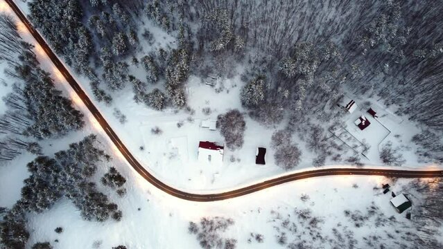 Amazing evening aerial view from drone on road between scenic mountains in winter. Top-down view of a picturesque mountain serpentine and cozy snow-covered houses. Magic winter landscape