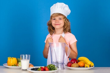 Child wearing cooker uniform and chef hat preparing vegetables on kitchen, studio portrait. Cooking, culinary and kids food concept. Fruits and vegetables for kids.