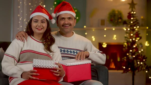 Happy couples with santa hata with gift boxes looking camera during christmas holiday celebration at home - concept of holidays, companionship and xmas holidays