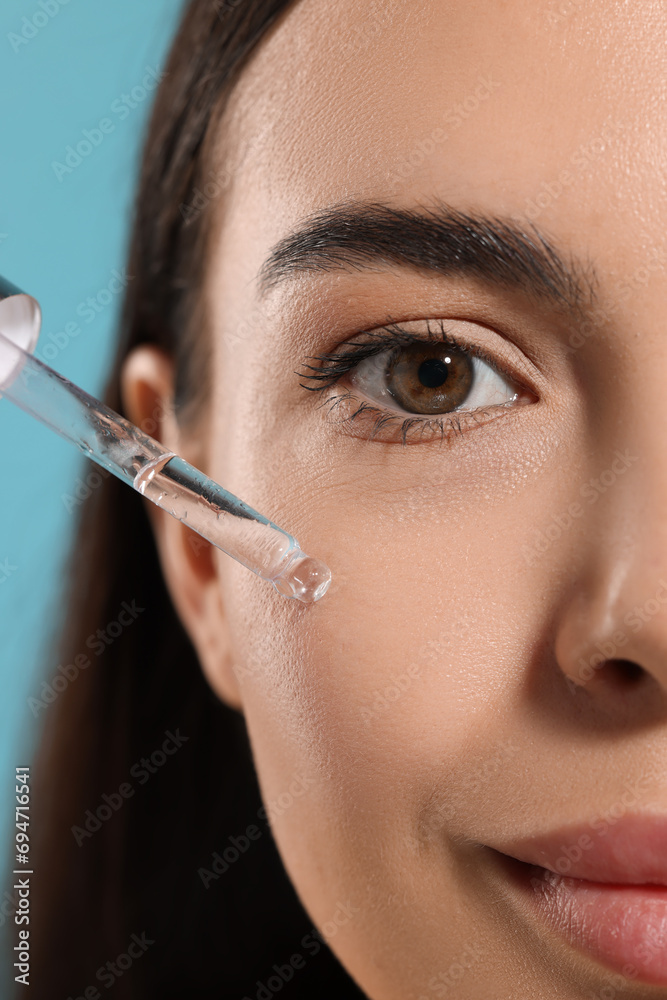 Canvas Prints Beautiful young woman applying serum onto her face on light blue background, closeup