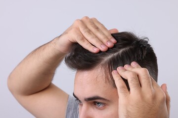 Fototapeta premium Man examining his head on light grey background, closeup. Dandruff problem