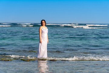 Fototapeta na wymiar Beautiful woman in a white dress on the beach on a sunny day in summer.