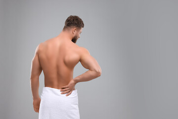 Man suffering from back pain on grey background, back view. Space for text