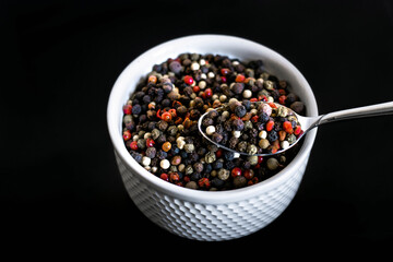 A mixture of pepper varieties with peas on the white plate on the black background. Heap of various pepper. Mix of red, black and white peppercorn seeds isolated on white. Top view