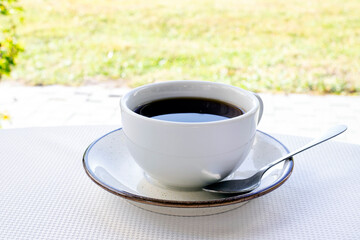 A white cup of coffee close-up is on the table against the backdrop of the river. Tea party in nature. Coffee morning
