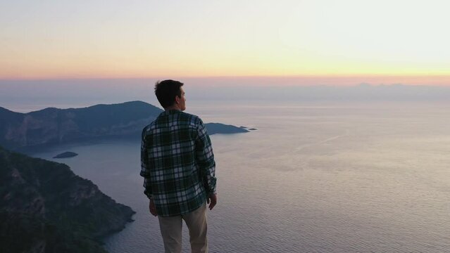 Young man standing on top of the mountain and enjoying scenery sunset view over sea 