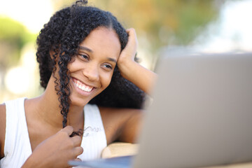 Happy black woman playing with hair watching media on laptop