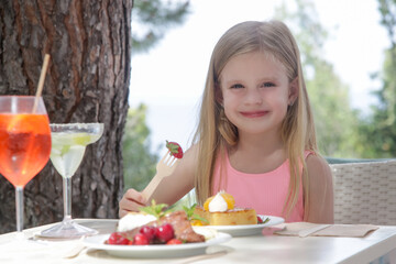 Cheerful little girl eating cake at the outdoor cafe	