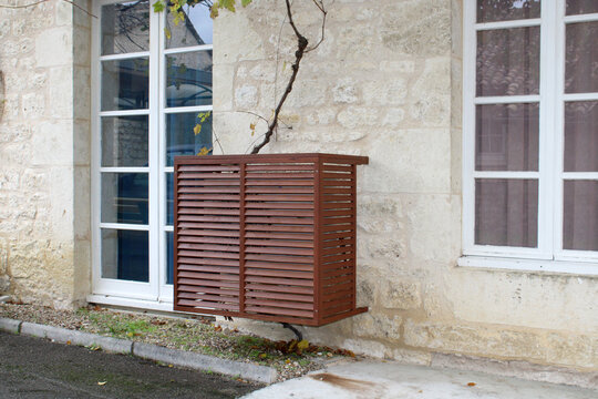 Habillage bois d'un climatiseur extérieur, cache groupe extérieur effet bois sur façade de maison en pierre