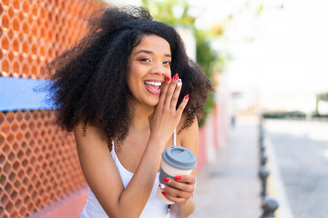 Young African American woman holding a take away coffee at outdoors whispering something