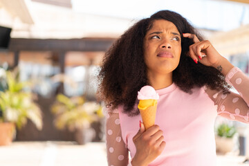 Young African American woman with a cornet ice cream at outdoors having doubts and with confuse face expression
