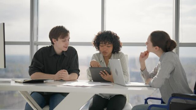 Paralyzed woman works with colleagues. Female in wheelchair has spine legs trauma discussing working project in office on meeting with multiethnic team. Teamwork, brainstorming, special needs person.