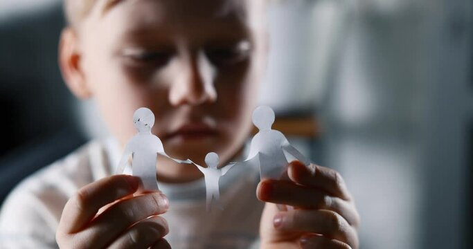 little sad boy with paper family in hands. concept of family issues, divorce, custody and child abuse