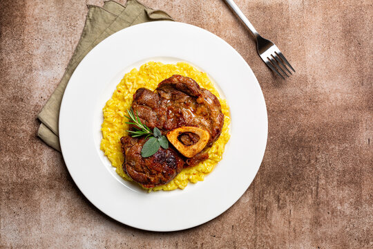 Top view of plate with Italian dish Ossobuco, braised meat served with saffron risotto alla milanese, specialty of Lombard cuisine. Brown background.