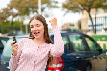 Young pretty blonde woman holding car keys at outdoors celebrating a victory