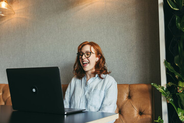 Ginger-haired businesswoman smiling during a productive online meeting at a cozy café